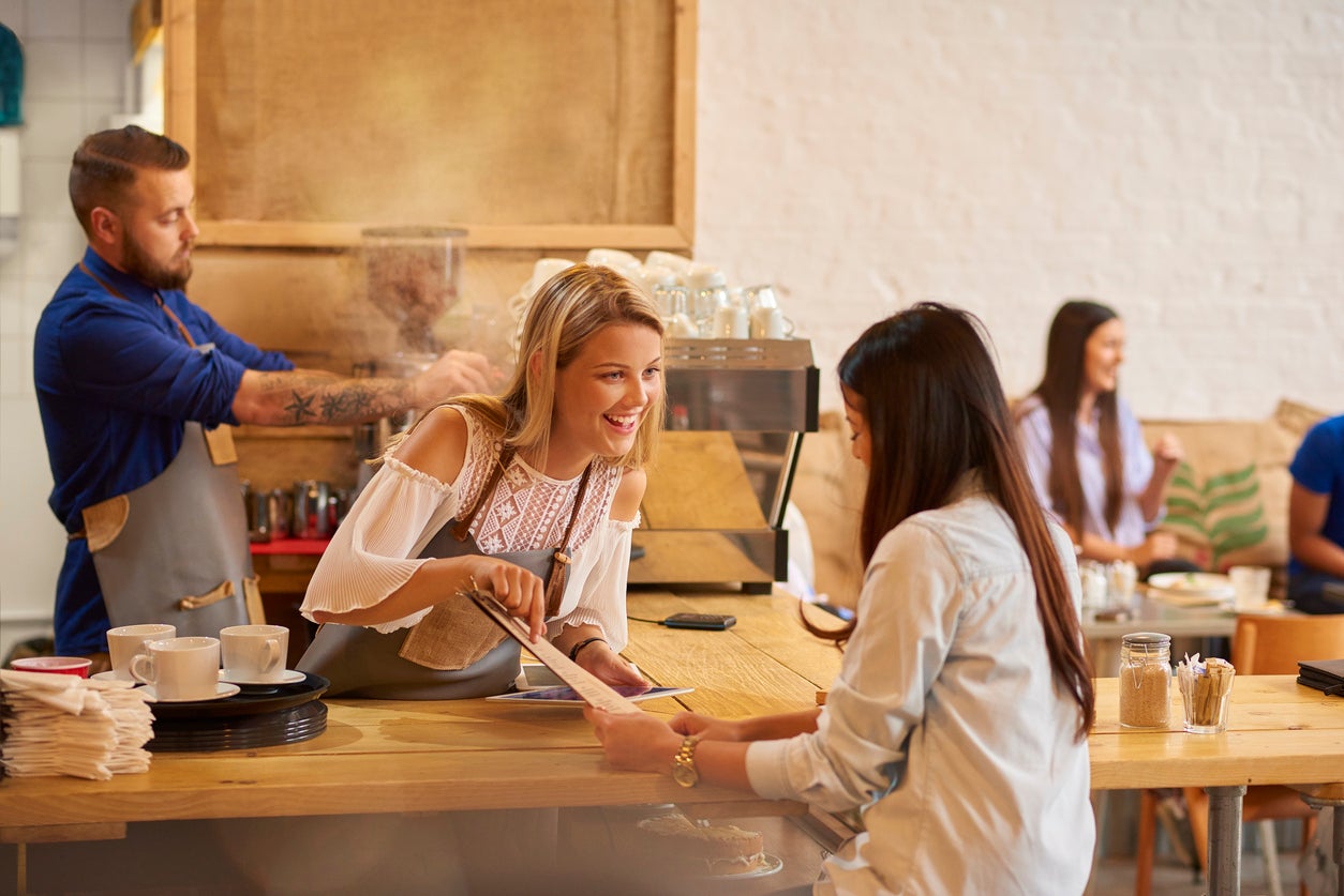 a coffee shop worker smiles at the customer as she recommends her favourite thing on the menu . In the background a male colleague is making coffee and other customers can be seen having fun